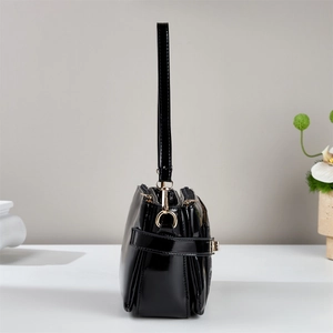 Detail view of the black patent leather shoulder bag showing zipper layers and gold hardware