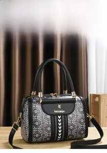 Detail der Boston Bag mit schwarz-weißem Muster und Metalllogo auf einem Holztiisch