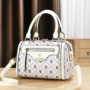 Beige Boston bag with logo pattern, dual handles and gold hardware on wooden surface