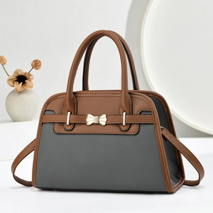 Détail du sac à main en cuir grainé avec nœud doré métallique et couleurs contrastées