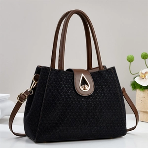 Close-up of black woven texture handbag with golden teardrop buckle and leather trim