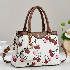 Elegant white tote bag with red cherry prints and brown leather handles on a white table