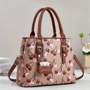 Chic beige tote bag with cherry print, brown leather handles and a mini bag charm