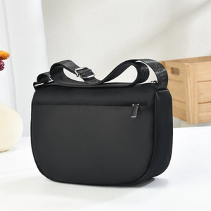 Black nylon crossbody bag with wide adjustable strap on a minimalist home background