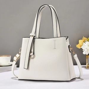 Borsa tote minimalista in pelle beige con finiture dorate e tracolla regolabile sul tavolo