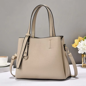 Dettaglio borsa beige a grana di litchi con finiture dorate su superficie bianca