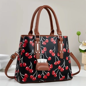 Elegant black handbag with cherry print and brown leather handles on a white surface