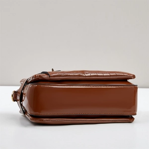 Detail of brown faux crocodile leather bag showing side view and golden hardware