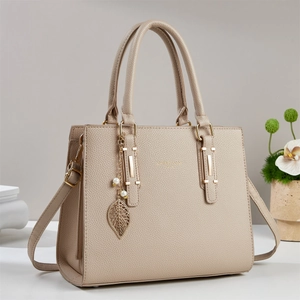 Elegante borsa a mano beige testurizzata con ciondolo a foglia dorata e perla