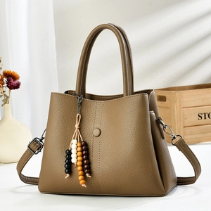 Khaki pebbled leather handbag with wide strap and beaded tassel on wood background