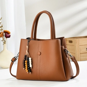 Brown lychee leather handbag with wide shoulder strap and wooden bead tassel accessory