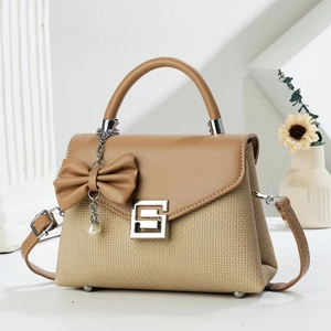 Minimalist tan tote bag with textured body, pearl bow detail, and adjustable shoulder strap