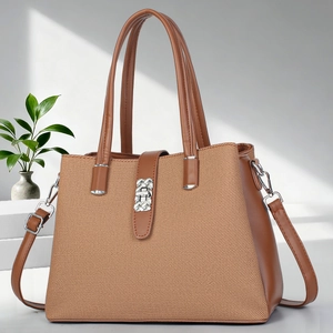 Brown leather and canvas tote bag with silver buckle on a minimalist white platform