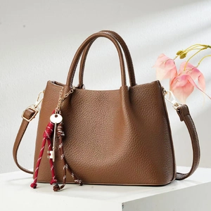 Detail of a dark brown pebble leather handbag featuring gold hardware and a tassel keychain