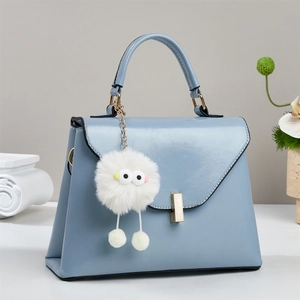 Minimalistische hellblaue Handtasche mit süßem Monster-Plüschanhänger und Gold-Details