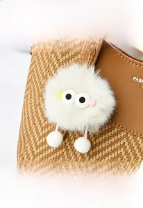 Detail of cute white plush ball charm with large eyes on a brown woven texture bucket bag