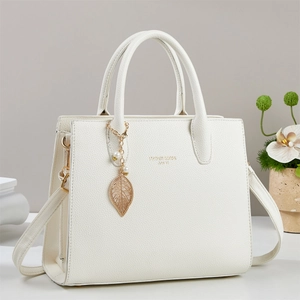 Detail der cremeweißen Handtasche mit goldenen Beschlägen und Perlenanhänger