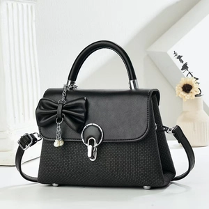 Elegant black bow handbag with woven texture and pearl pendant on a minimal background