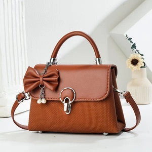 Detail of caramel brown crossbody bag with woven texture, bow, and pearl chain pendant