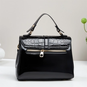 Detail of glossy black patent leather handbag with crocodile pattern and gold hardware