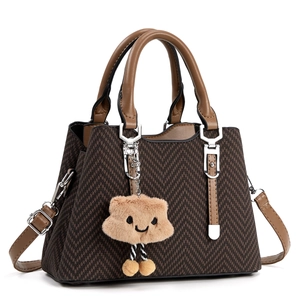 Close-up of dark brown woven texture handbag with light brown leather trim and plush charm