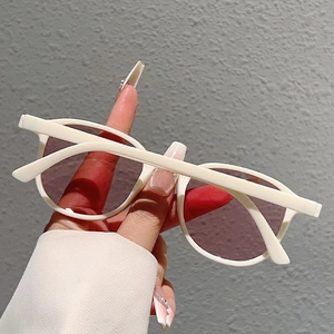 Detail view of white oversized round sunglasses with dark lenses held by a hand