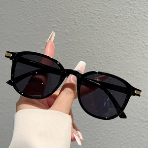 Detail of oversized black sunglasses featuring golden vertical metal trim on the hinges