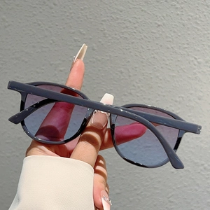 Detail view of oval plastic sunglasses with blue-purple gradient lenses held by hand
