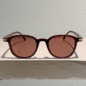Detail of dark red sunglasses with translucent frame and gold hinge accents
