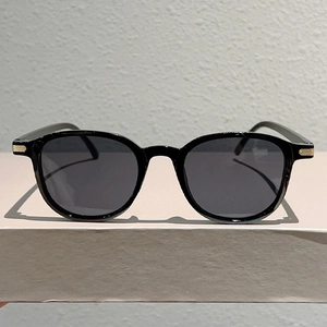 Polished black plastic round sunglasses with golden temple hinge detail and gray lenses