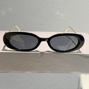 Vue détaillée des lunettes de soleil ovales noires avec branches dorées sur socle