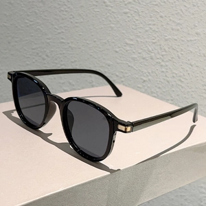 Detail of minimalist black round sunglasses featuring elegant golden metal temple accents