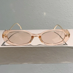 Détail de lunettes de soleil ovales roses avec monture transparente et branches dorées