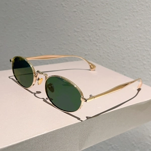 Dettaglio di occhiali da sole ovali vintage con montatura dorata e lenti verde scuro su base
