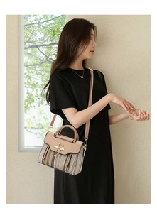 Detail of crossbody bag with gold swan buckle and textured beige woven paneling