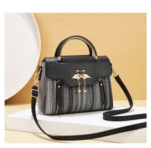 Detail of striped crossbody bag featuring golden heart clasp with a pearl pendant chain