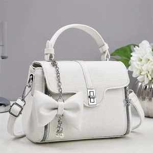 Close-up of white crossbody bag with decorative pearl bow and silver metallic lock detail
