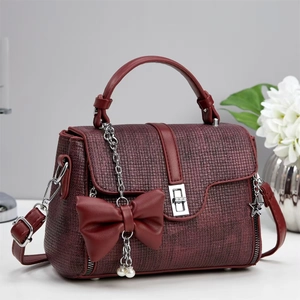 Detailed view of burgundy tweed handbag with leather strap and pearl bow charm