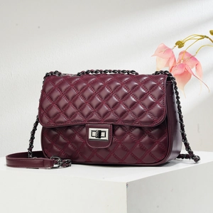 Detailed view of burgundy quilted crossbody bag with silver lock and chain strap