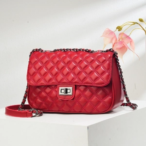 Close-up of red quilted leather shoulder bag with silver chain and twist lock on white stand