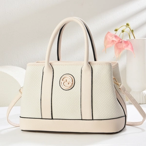 Beige woven tote bag with leather trim and gold logo on minimalist background