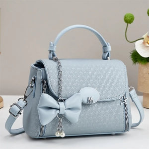 Close-up of light blue textured shoulder bag with M metal logo and pearl bow charm detail