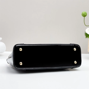 Detail view of the bag's glossy black crocodile embossed base with four gold metal studs