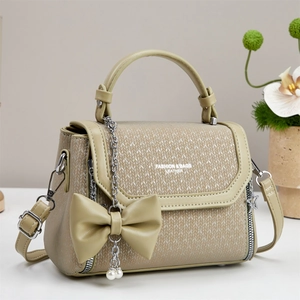 Close-up of khaki shoulder bag with woven texture, bow charm, and metal chain details