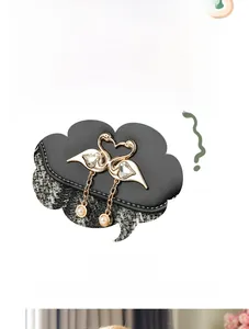 Detail of golden swan heart hardware with crystal inlay and pearl on black leather bag