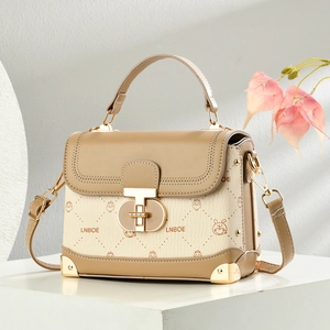 Elegante Schultertasche in Beige-Braun mit goldenen Metallecken auf weißem Podest