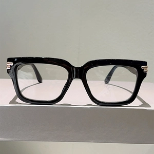 Close-up of black oversized glasses with gold metal accents on a grey geometric block