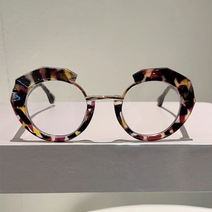 Irregular round tortoise shell glasses with gold metal accents on a gray display block