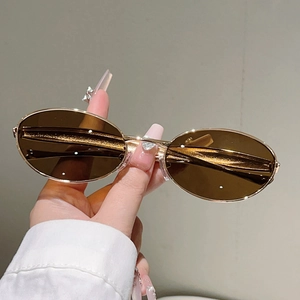 Détail de lunettes de soleil ovales avec monture dorée et verres marron en main
