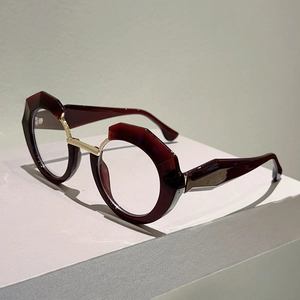 Detail of burgundy geometric eyewear frame featuring gold metal bridge and hinges